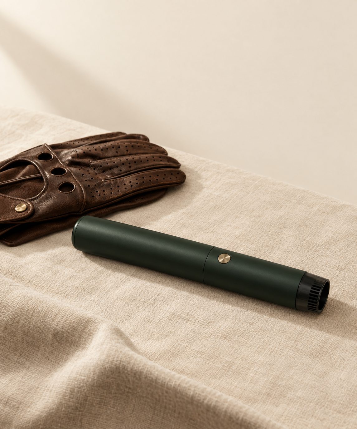 AERIKAI A-020, a slim pen-form car vacuum in matte forest green with a small brushed brass button, resting beside brown leather driving gloves.